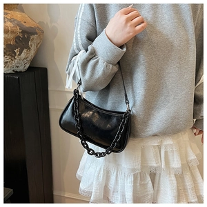 Detail of black patent leather baguette bag featuring thick chain strap and sleek finish