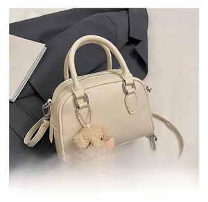 Detail of cream pebbled leather pillow bag with silver hardware and plush dog charm
