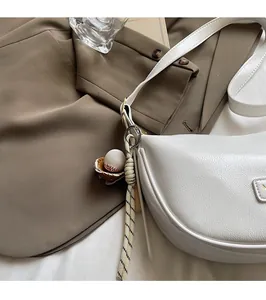 Détail du sac demi-lune blanc en cuir souple avec pendentif de baseball et boucle dorée
