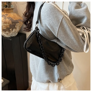 Detail of black patent leather baguette bag with thick chain worn over the shoulder