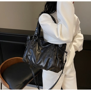 Detail of black pleated faux leather tote bag with silver studs and adjustable strap