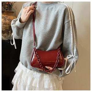 Detail of red patent leather crossbody bag with chunky chain strap and sleek glossy finish
