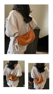 Détail du sac croissant caramel avec pendentif baseball et texture en cuir souple plissé