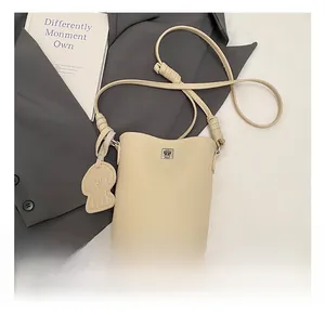 Dettaglio borsa a secchiello beige grana litchi con chiusura a scatto e ciondolo a cane
