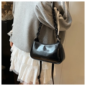 Detailed close-up of glossy black chain dumpling bag with adjustable strap on a model