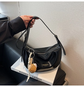 Détail du sac demi-lune en cuir verni noir avec plaque métallique et breloques de sport