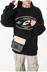 Close-up of cream and black crossbody tech bag with mesh pocket on streetwear outfit