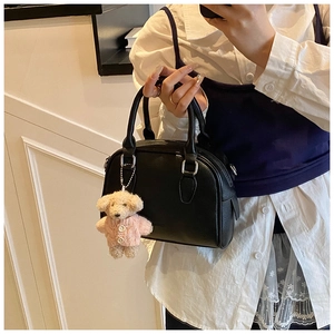 Detail of black pebbled leather handbag featuring a cute plush bear charm and silver hardware