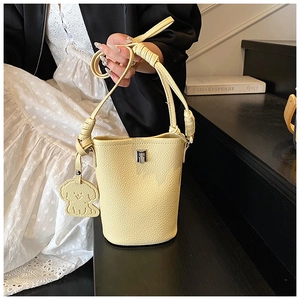 Dettaglio della borsa a secchiello in pelle giallo crema con texture litchi e ciondolo