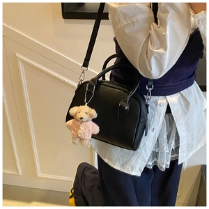 Detail of black pebbled leather bowling bag with a cute teddy bear charm accessory