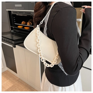 Detail of white leather dumpling bag with chunky chain strap on a kitchen backdrop