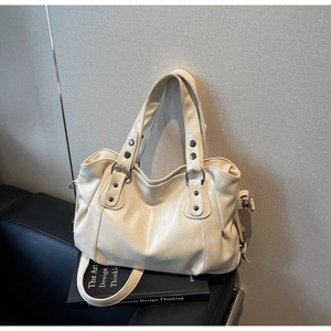 Detail of a creamy white PU leather tote bag with silver studs on a black leather seat