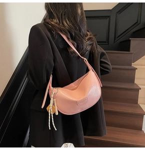 Sac à épaule demi-lune rose en cuir grainé avec détail de gland sur des escaliers