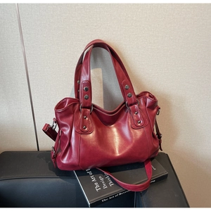 Close-up of burgundy leather tote bag featuring metallic rivet details and adjustable strap