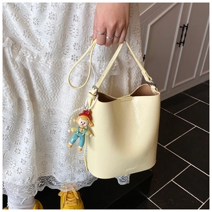 Detail of light yellow leather bucket bag with MULOO logo and cute cartoon doll charm