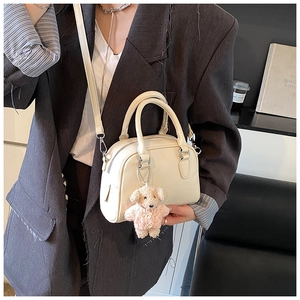 Close-up of cream textured leather pillow bag with cute bear charm and shoulder strap