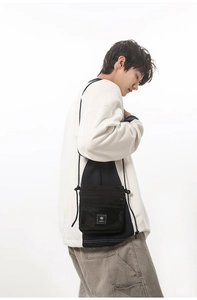 Close-up of black nylon crossbody bag with mesh zip pocket and logo label detail