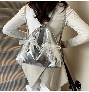 Silver metallic backpack with lace bows and pearl charms shown on a model's back