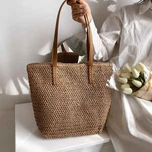 Gros plan détaillé d'un sac cabas en paille tissé avec anses en cuir marron et coutures
