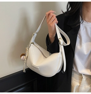 Détail du sac demi-lune blanc avec texture litchi et pendentif baseball sur la bandoulière