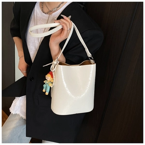 Detail of a creamy white bucket bag with a glossy texture and a cute cartoon charm