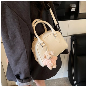 Detail of beige lychee textured pillow bag with a small teddy bear charm on shoulder strap