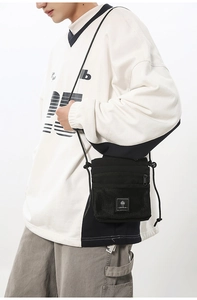 Detail of black canvas techwear crossbody bag with mesh pocket and logo tag on model