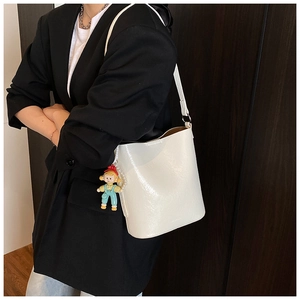 Detail of white glossy bucket bag with doll pendant on a side-wearing model