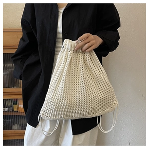 Detailed crochet texture of off-white hollow woven drawstring bag held by model