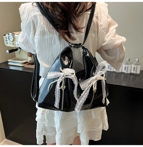 Detail of black patent leather backpack with white lace bow and pearl heart charm