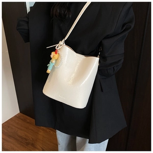 Detailed view of cream patent leather bucket bag with brand logo and cute doll charm