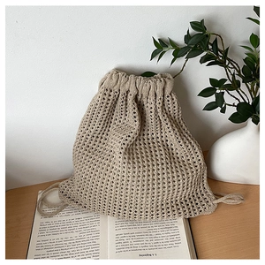 Detail of beige knit drawstring bucket bag with mesh texture and natural cotton rope
