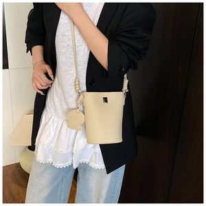 Dettaglio borsa a tracolla crema con ciondolo su un blazer nero alla moda
