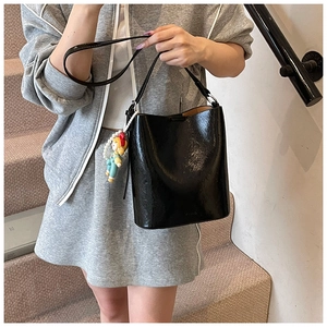 Detail of a shiny black bucket bag with a colorful plush charm on long strap