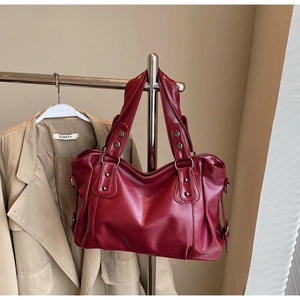 Close-up of deep red leather tote bag with metal rivets and adjustable side straps