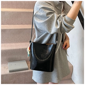 Fashionable black glossy bucket bag with a colorful charm shown on a casual staircase
