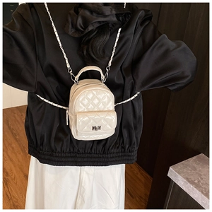Mini cream white quilted backpack with chain straps shown on a model in a minimalist setting