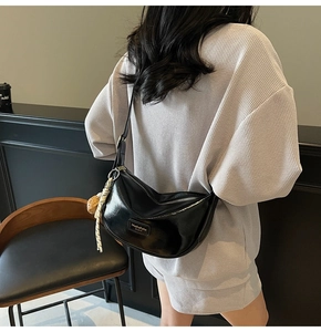 Détail d'un sac demi-lune en PU noir montrant le fini brillant et le pendentif pompon