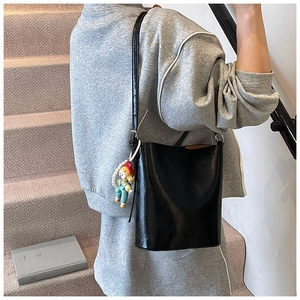 Side view of black glossy bucket bag with doll charm and pearl chain on a model