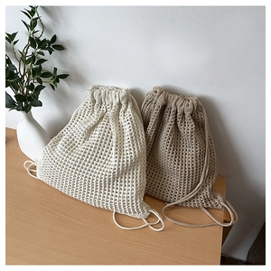Detail of hollow knitted drawstring backpacks in beige and light brown on a wooden surface