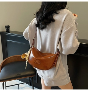 Détail du sac demi-lune marron brillant avec logo et pendentif à franges