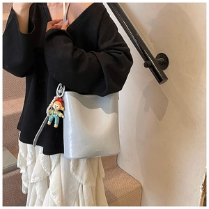Close-up of shiny silver bucket bag with MICOC logo and cute pearl doll charm