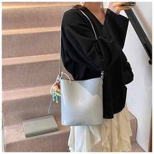 Detail of light blue bucket bag with MUDUO logo and cute cartoon doll pendant