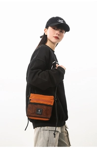 Detail of orange techwear crossbody bag with black mesh pocket and logo on black outfit
