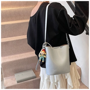 Detail of silver bucket bag with logo engraving and cute doll pendant on leather