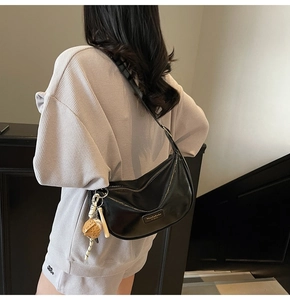 Gros plan du sac demi-lune en similicuir noir avec boucles argentées et pompon décoratif