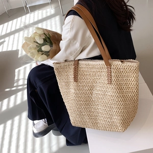 Détail d'un sac cabas tissé beige avec anses en cuir marron et fermeture éclair métallique sûre