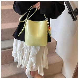 Detail of glossy yellow bucket bag with pearl bear charm worn as a crossbody