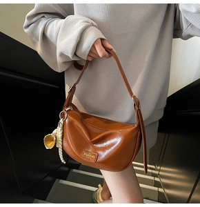 Détail d'un sac demi-lune en cuir brillant marron avec fermeture éclair et breloque
