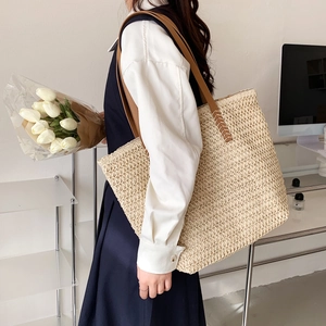 Détail d'un cabas en paille tissée avec bandoulière en cuir marron et coutures en croix